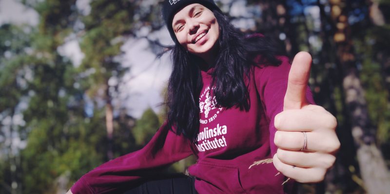 Annmari har på sig en Karolinska Institutet hoodie, visar tummen upp och ler
