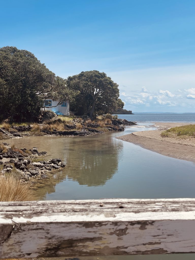 little bay with sea in the background and a white and blue cottage on the left taken from a bridge