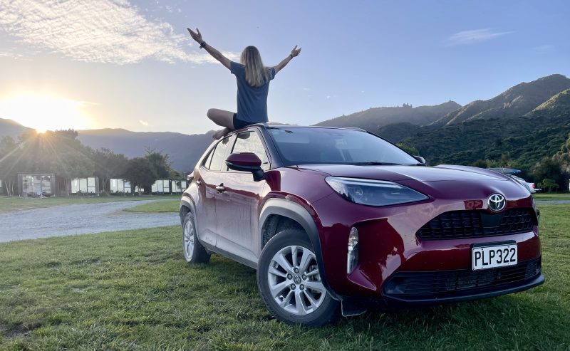 girl sitting on top of a car with mountains in the background