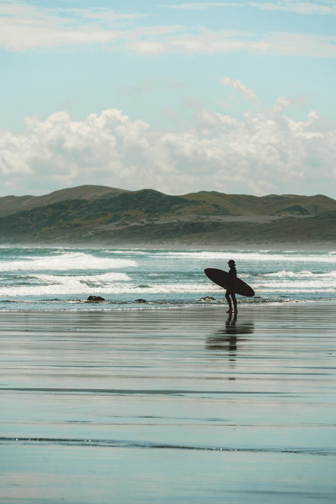 A surfer on the beach holding his board with waves in the background