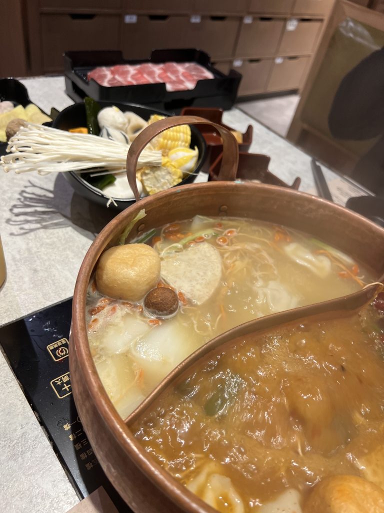 Hot pot with two different flavours and vegetables in the background
