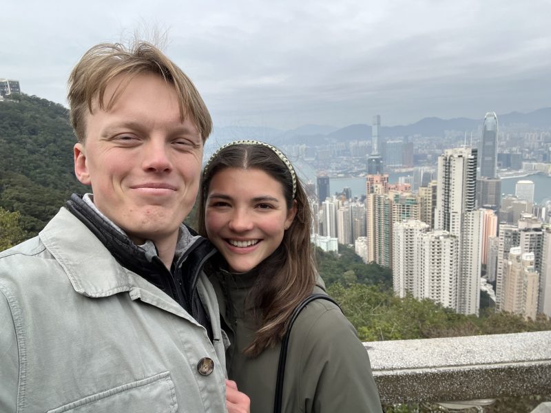 A couple standing on a viewing platform at the Peak with the skyline of Central behind them in the distance.