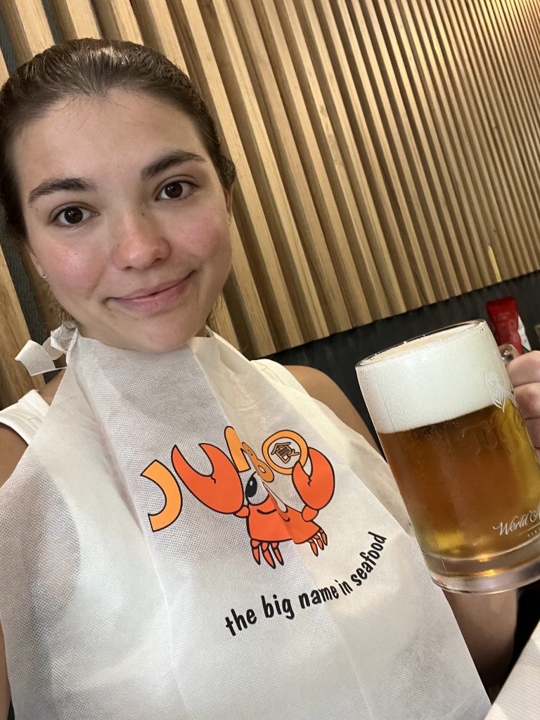 A girl wearing a bib with an orange logo including a smiling crab and holding a jug och beer, smiling for the camera