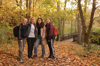 Group of four friends standing in a row smiling at the camera in a fall forest landscape