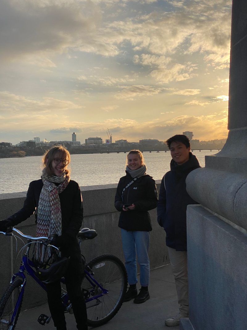 Three people standing in front of the skyline of Boston, one with a bike.