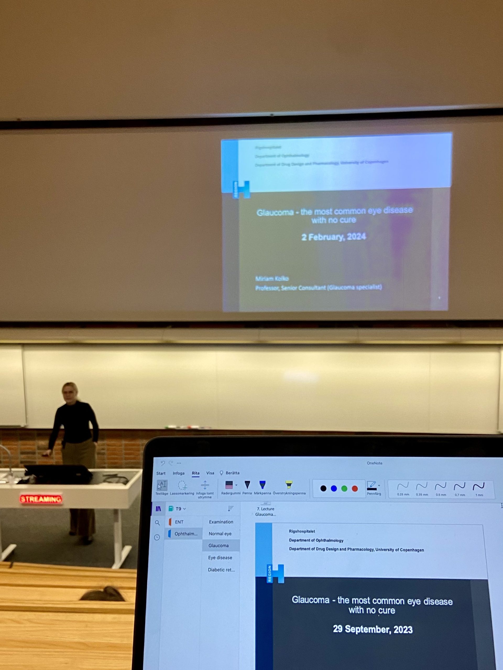 En föreläsningssal med lektor och en dator med glaukomföreläsning på skärmen