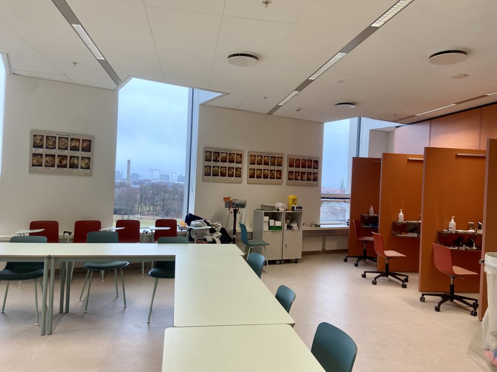 Ett klassrum med bord och stolar samt bås med undersökningsmaterial längs högra väggen