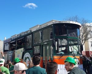 A green Hop-On-Hop-Off bus driving through the crowd as part of the parade.