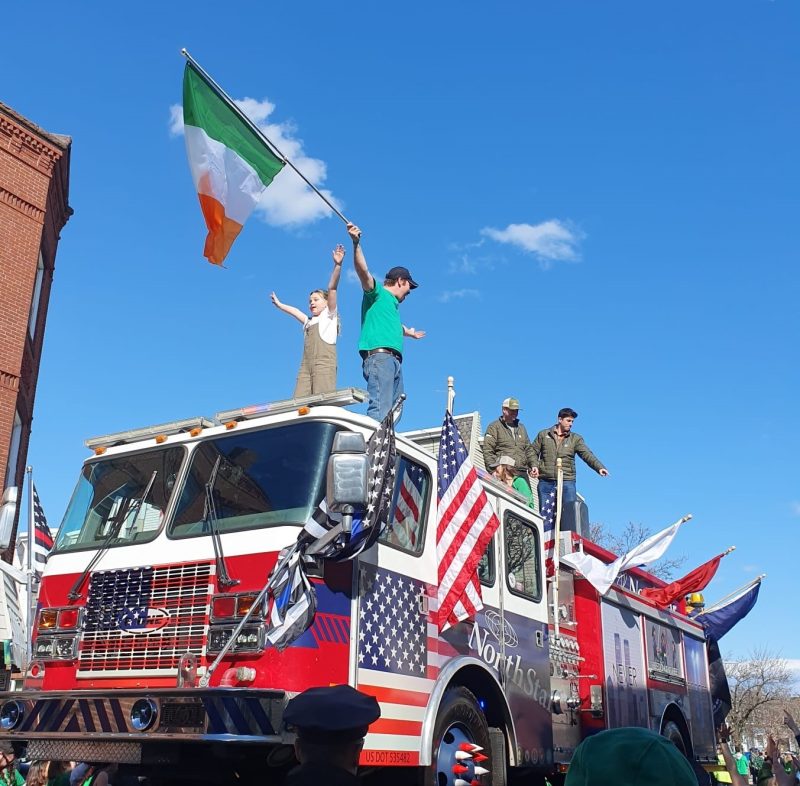 Float consisting of a truck decorated in the colors of the American flag with five people on it, one of them waving the Irish flag.