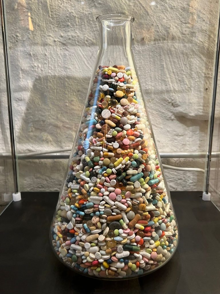 A large glass beaker containing hundreds of colorful pills.