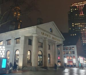 A gray building with four columns at the entrance and golden lettering reading Quincy Market.