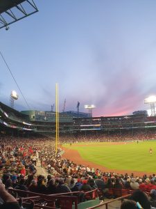 View from inside a baseball stadium with a red sunset in the background behind the field.