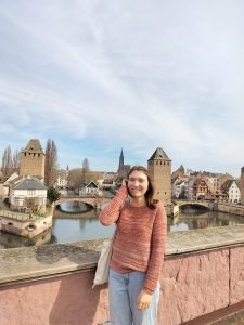 Girl standing on a bridge in front of a river lined with houses.