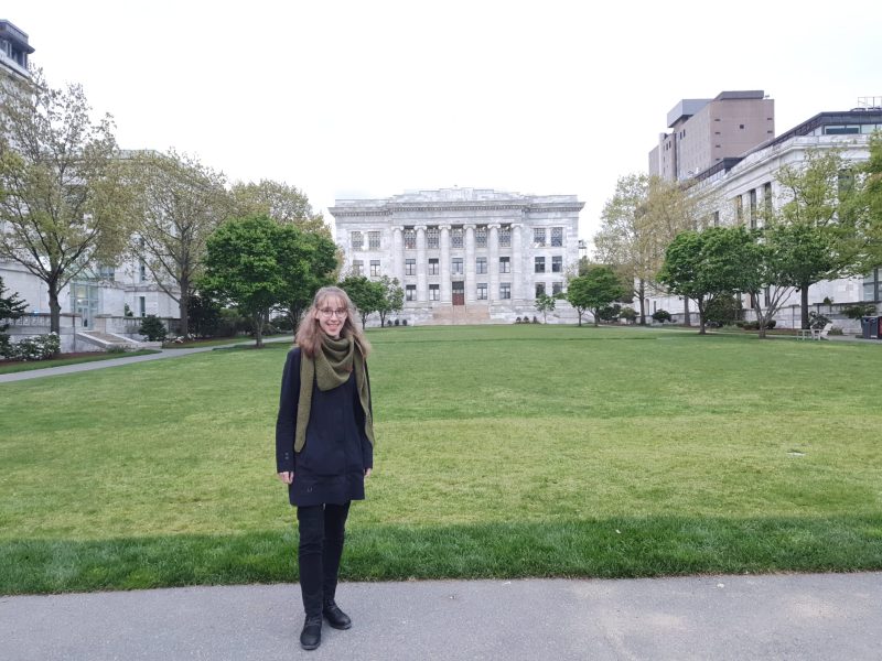 Girl standing in front of a lawn surrounded by white and gray marble buildings, smiling at the camera.