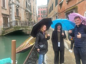 Three people standing next to one of the Venice canals holding umbrellas.